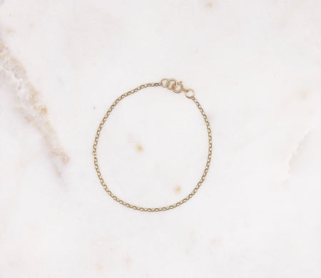 A fine gold chain bracelet displayed on a marble board.