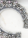 A luxurious grey silk velvet headband heavily adorned with high quality light and dark grey glass pearls and clear crystals of varying sizes displayed on a marble board.