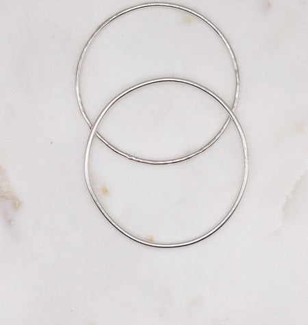 Two fine organically shaped circular silver bangles displayed on a marble board. One bangle is smooth while the other is lightly textured.