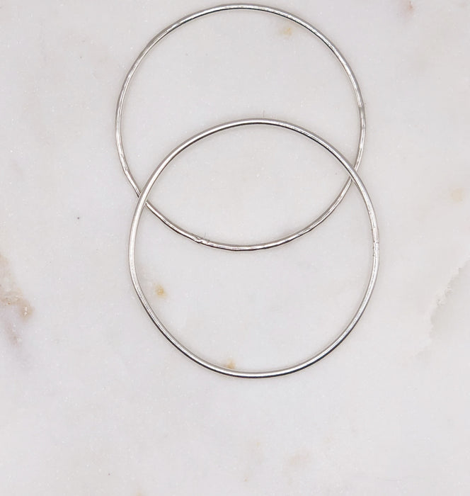 Two fine organically shaped circular silver bangles displayed on a marble board. One bangle is smooth while the other is lightly textured.