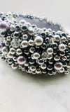 A close up photograph of a luxurious grey silk velvet headband heavily adorned with high quality light and dark grey glass pearls and clear crystals of varying sizes displayed on a marble board.