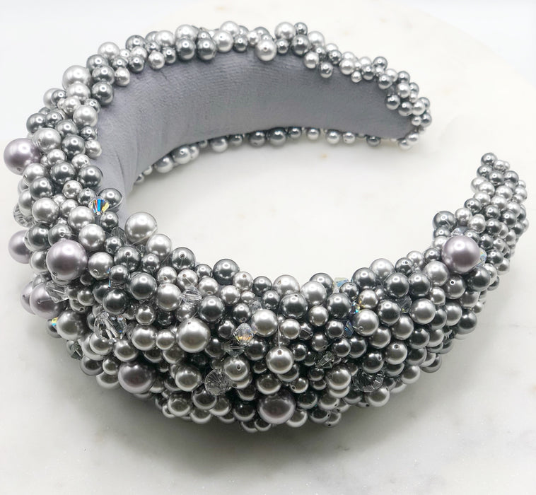 A luxurious grey silk velvet headband heavily adorned with high quality light and dark grey glass pearls and clear crystals of varying sizes displayed on a marble board.