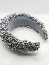 A luxurious grey silk velvet headband heavily adorned with high quality light and dark grey glass pearls and clear crystals of varying sizes displayed on a marble board.