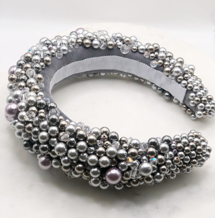 A luxurious grey silk velvet headband heavily adorned with high quality light and dark grey glass pearls and clear crystals of varying sizes displayed on a marble board.