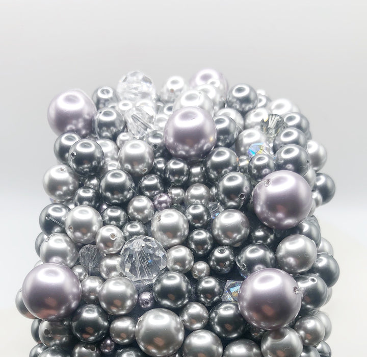 A close up photograph of a luxurious grey silk velvet headband heavily adorned with high quality light and dark grey glass pearls and clear crystals of varying sizes displayed on a marble board.