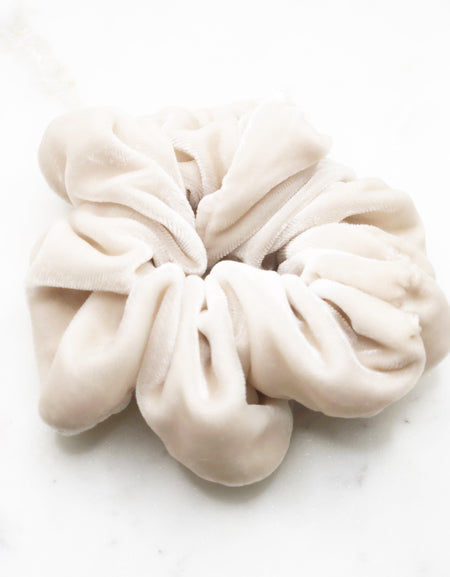 A luxurious pale pink silk scrunchie displayed on a marble board.