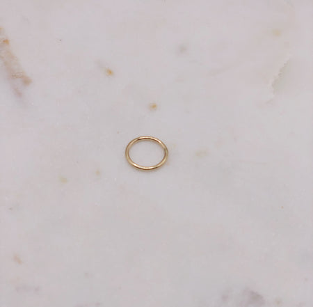 A petite yet solid gold ring made from round gold wire displayed on a marble board.