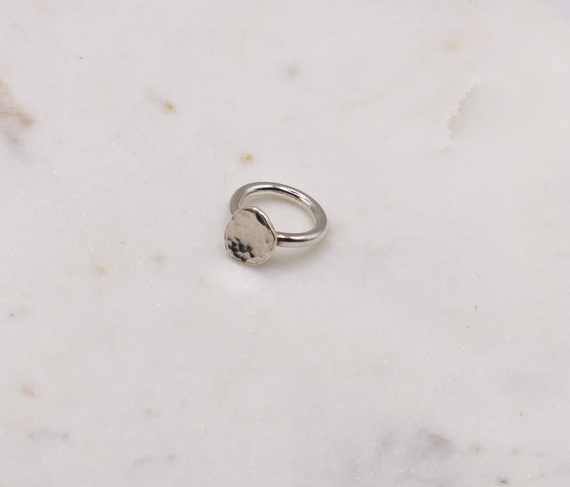 A chunky silver ring consisting of a 3mm silver wire band with a lightly textured circular silver nugget/pebble attached. Sat on a marble board.