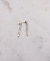 A pair of silver earrings each measuring around 4cm long and lightly textured to resemble that of a twig displayed on a marble board.