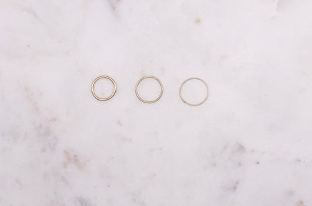 A trio of gold rings in three different thicknesses displayed on a marble board.