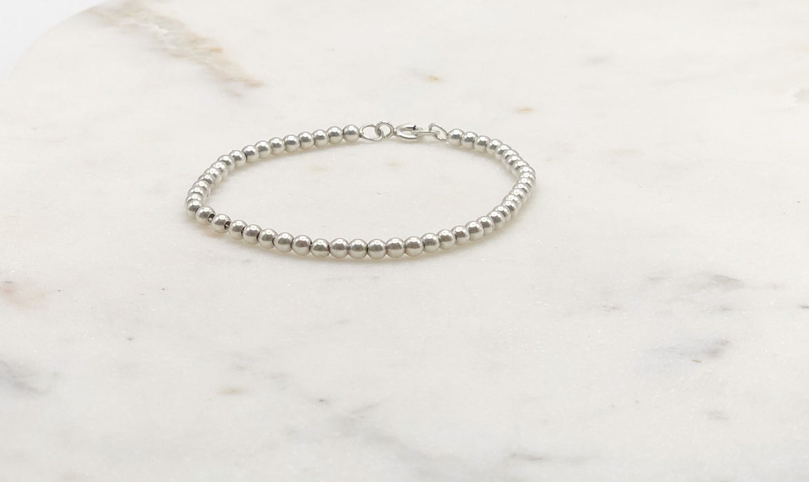 Silver beaded bracelet displayed on a marble board.