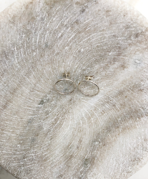 An overhead close up photograph of a pair of silver hoop studs lightly textured displayed in a shallow marble bowl. The earrings measure approximately 2cm each in diameter.