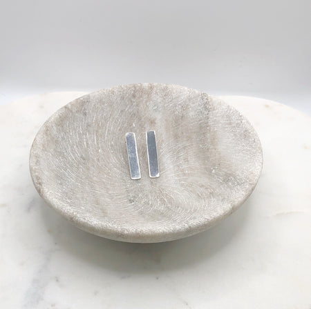 A pair of silver rectangular earrings lying next to each other in a shallow marble bowl.