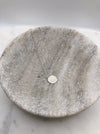 A lightly textured circular silver pendant attached to a medium weight chain displayed in a marble bowl.