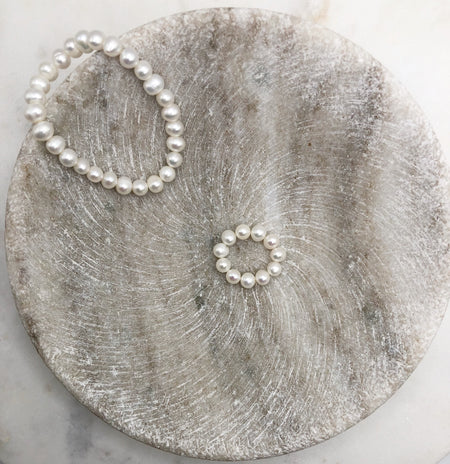 A white pearl bracelet and ring both made from Fresh Water Pearls displayed in a shallow marble bowl.