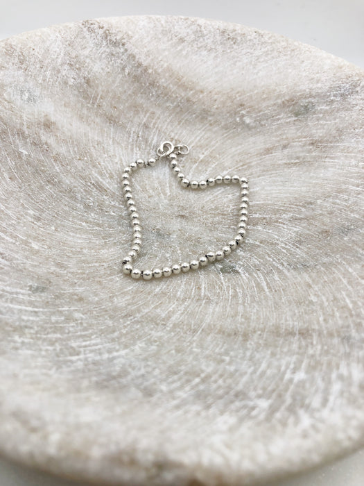 Silver beaded bracelet lying in a shallow marble bowl.