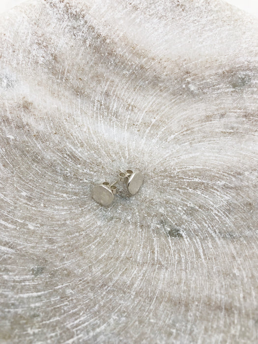 A pair of organically formed small circular silver studs displayed in a shallow marble bowl.