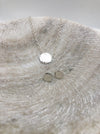 A lightly textured circular silver pendant attached to a medium weight chain and a pair of small silver studs in the same circular and textured design. Both displayed in a marble bowl.