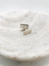 A pair of silver rectangle cufflinks with the letters F L J engraved on both cufflinks displayed in a shallow marble bowl.