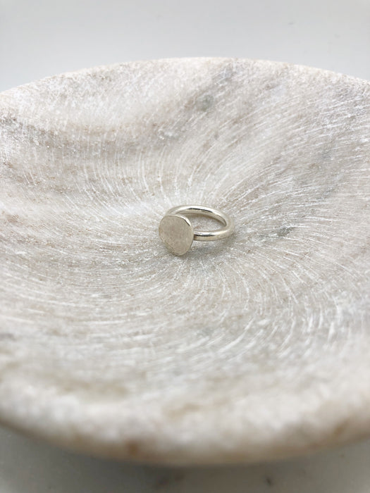 A chunky silver ring consisting of a 3mm silver wire band with a lightly textured circular silver nugget/pebble attached. Sat in a marble bowl.