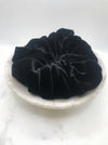 A luxuriously voluminous black silk scrunchie displayed in a marble bowl.