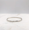 A lightly hammered organically shaped circular silver bangle displayed on a marble board.