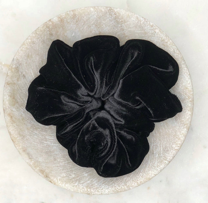 A luxurious black silk scrunchie displayed in a marble bowl.