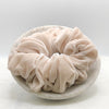 A luxuriously voluminous pale pink silk scrunchie displayed in a marble bowl.