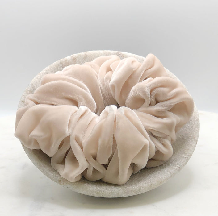 A luxuriously voluminous pale pink silk scrunchie displayed in a marble bowl.