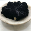 A luxurious black silk scrunchie with a circular gold tag with the letters FLJ engraved displayed in a marble bowl.