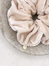 A luxurious pale pink silk scrunchie with a circular gold tag with the letters FLJ engraved displayed in a marble bowl.