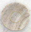 A slim organically shaped circular gold bangle smooth in texture and displayed in a marble bowl.