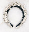 A luxurious black silk velvet headband heavily adorned with high quality white glass pearls and clear and black crystals displayed on a marble board.