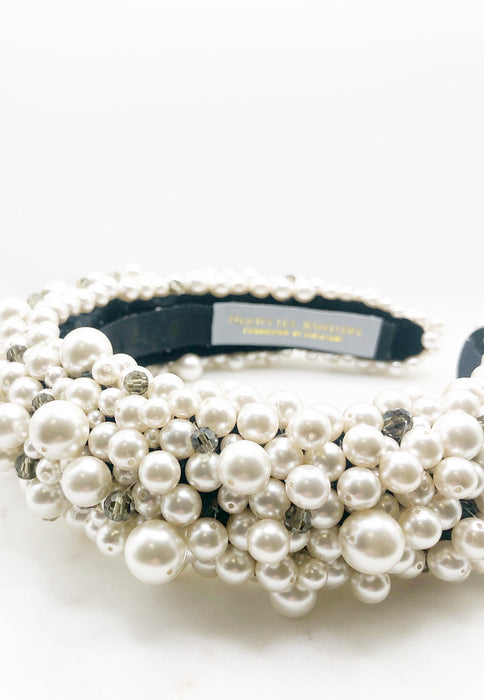 A luxurious black silk velvet headband heavily adorned with high quality white glass pearls and clear and black crystals with a grey label inside and the words FELICITY LEA JEWELLERY HANDMADE IN ENGLAND woven in gold metallic thread. displayed on a marble board 