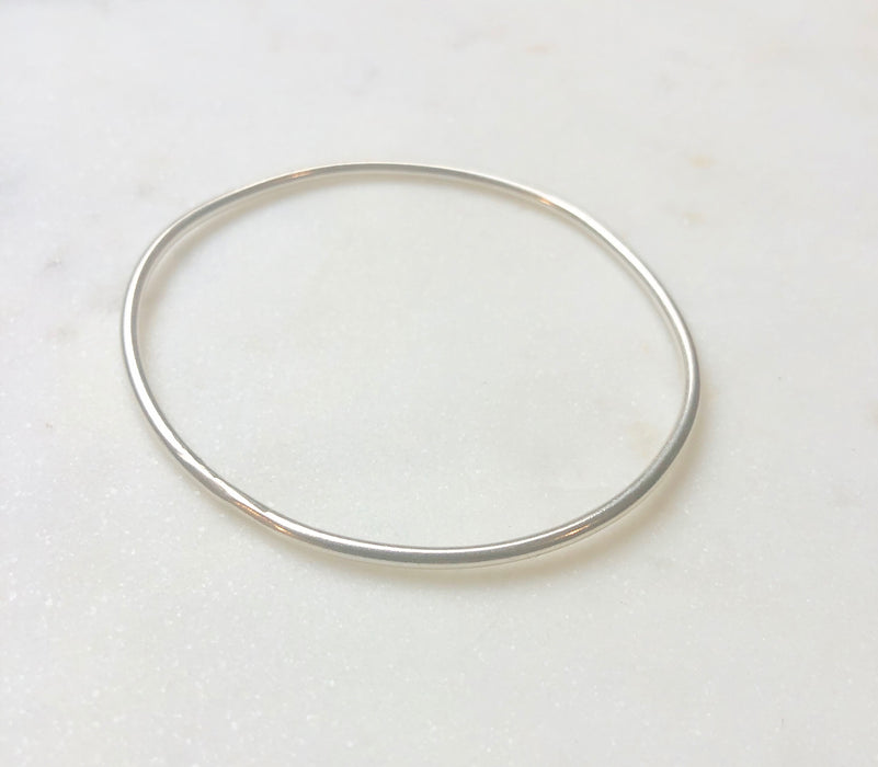 A smooth organically shaped circular silver bangle displayed on a marble board.